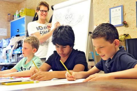 Robin Schicha (hinten) macht den Kindern vor, wie das Comiczeichnen funktioniert.Foto: Thomas Schmidt  Foto: Thomas Schmidt