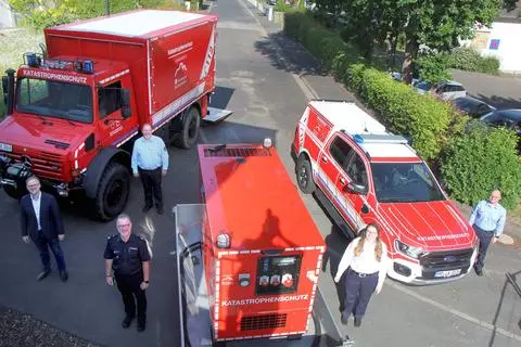 Landrat Jens Womelsdorf (l.) und Kreisbrandinspektor Lars Schäfer (vorne, li.) präsentieren gemeinsam mit Jörg Linne, Maria Müller und Tim Vollmerhausen (r.) vom Fachbereich Gefahrenabwehr die neue Ausrüstung auch für klimabedingte Einsätze. Um noch besser auch auf klimabedingte Einsätze vorbereitet zu sein, hat der Landkreis Marburg-Biedenkopf einen Mercedes-Unimog (li.), einen Ford Ranger (re.) sowie zwei neue Notstrom-Aggregate beschafft. Eines dieser Aggregate ist auf dem Bild zu sehen.