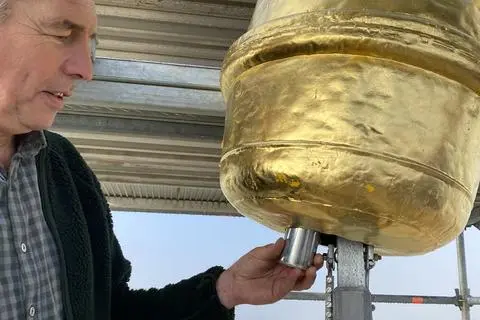 Schlosser Thomas Brühl, der das neue Kreuz angefertigt und den Hahn sowie die Kugel saniert hat, steckt die Zeitkapsel in die goldene Kugel. 