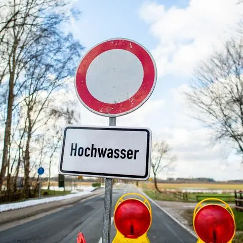 Eine Absperrbake und ein Schild mit der Aufschrift "Hochwasser" steht vor einer gesperrten Straße.