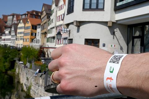 Eine Hand mit einem einem Armband mit einem Tagesticket für Tübingen nach einem Corona-Schnelltest liegt auf einem Brückengeländer vor der Kulisse einer historischen Häuserzeile.  Foto: dpa