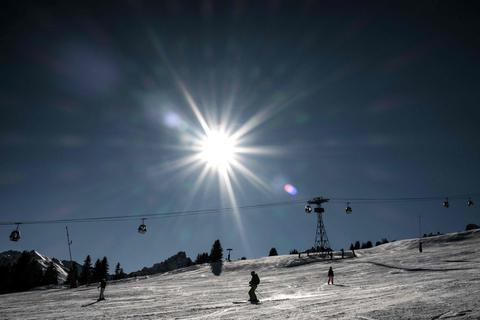 Die Sonne scheint auf die Piste während Skifahrer im Skigebiet einen Hang hinunter fahren. Foto: dpa/AFP | Jeff Pachoud