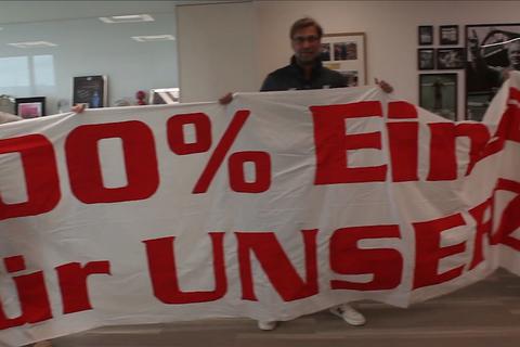 Jürgen Klopp und die Ultras halten das Banner im Büro des Liverpool-Trainers hoch. Screenshot: VRM 